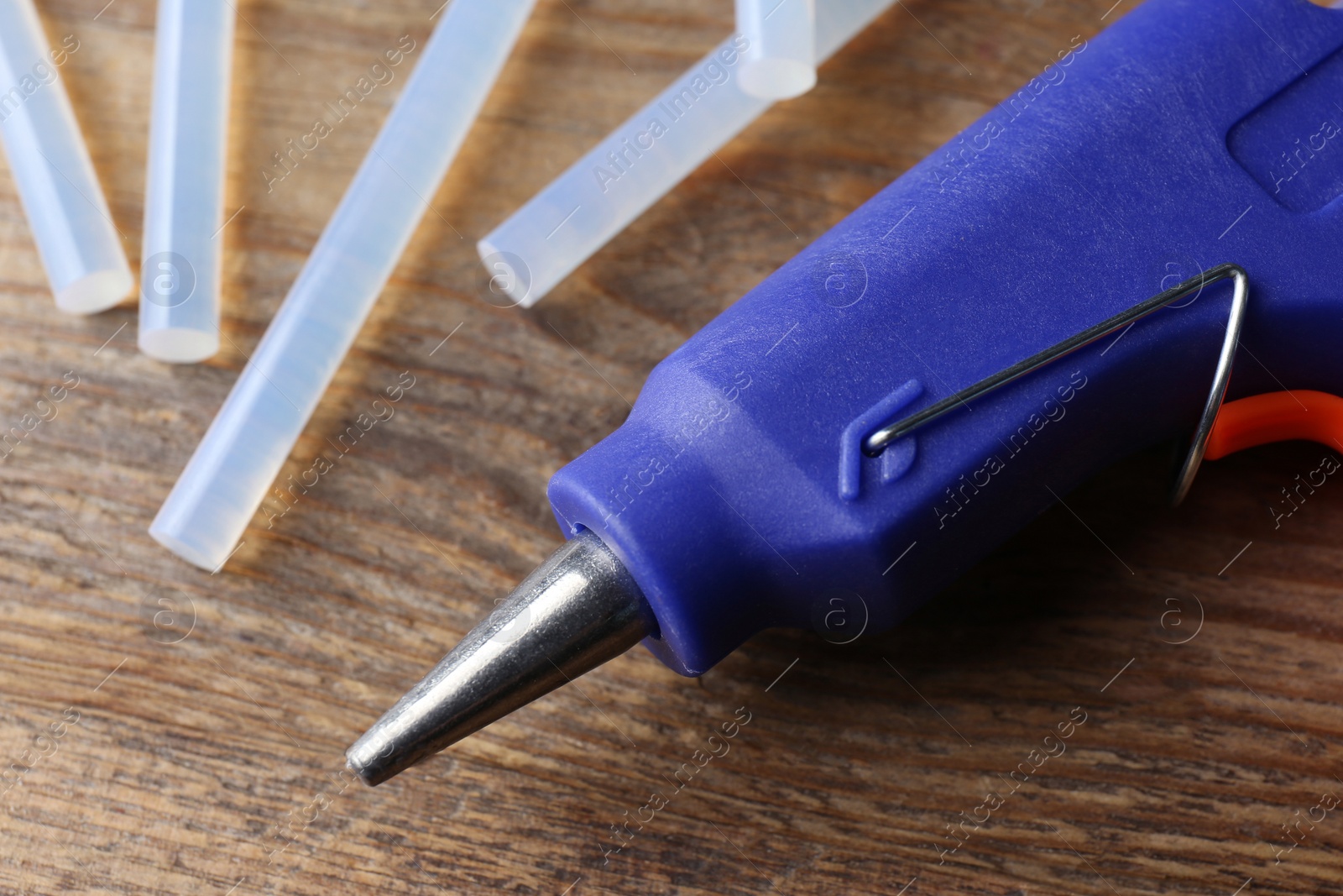 Photo of Hot glue gun and sticks on wooden table, closeup