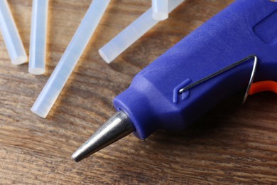 Hot glue gun and sticks on wooden table, closeup