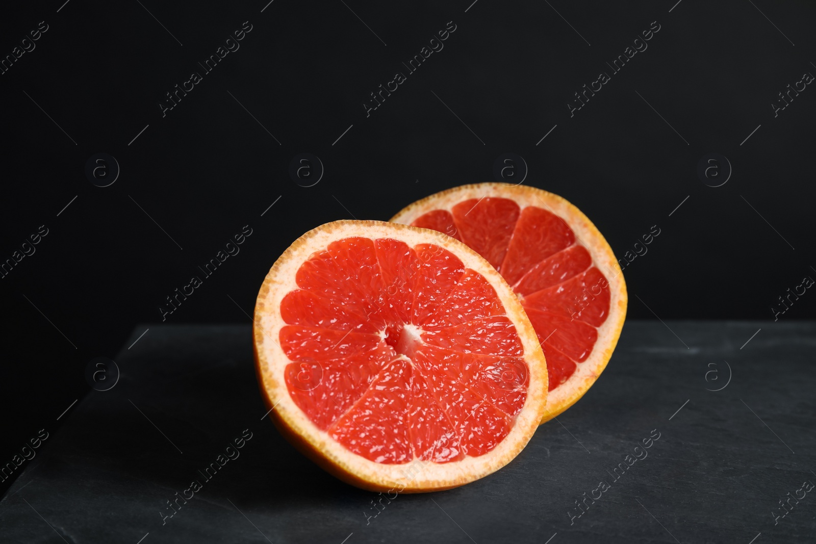 Photo of Halves of tasty ripe grapefruit on black background