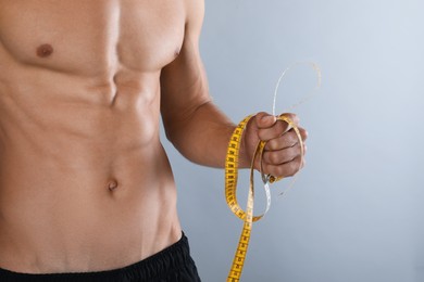 Photo of Shirtless man with slim body and measuring tape on grey background, closeup
