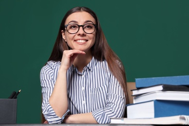 Portrait of young teacher at table against green background