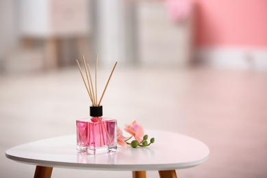 Aromatic reed air freshener and flowers on table against blurred background