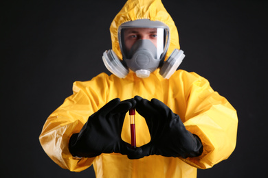 Photo of Man in chemical protective suit holding test tube of blood sample against black background. Virus research