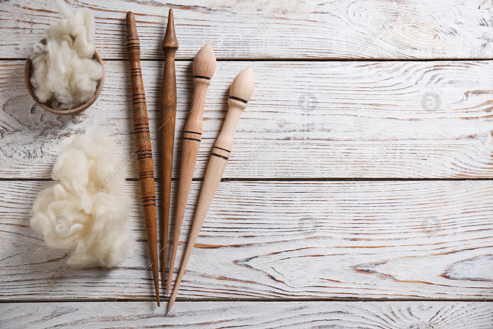 Photo of Soft wool and spindles on white wooden table, flat lay. Space for text