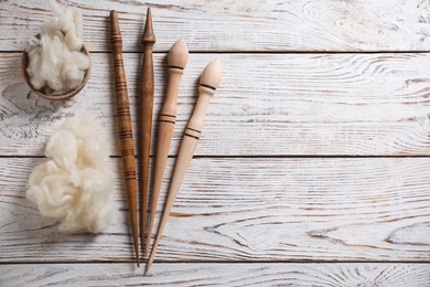 Photo of Soft wool and spindles on white wooden table, flat lay. Space for text