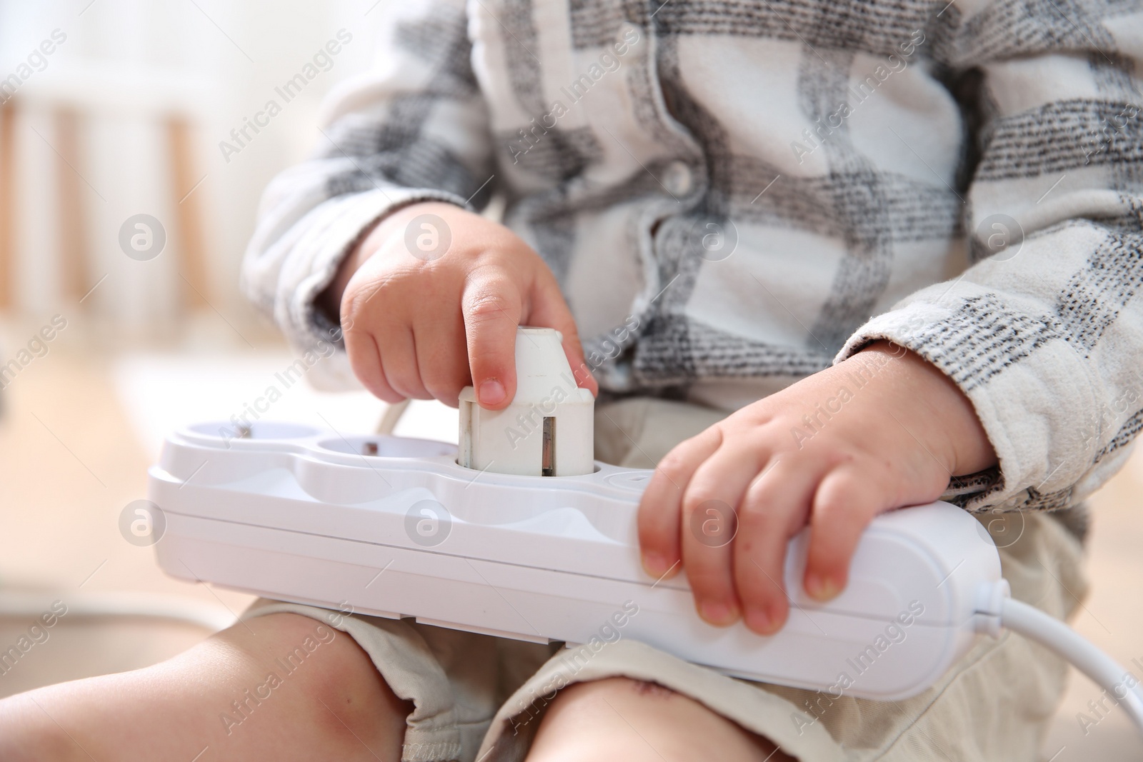 Photo of Little child playing with power strip and plug on floor indoors, closeup. Dangerous situation