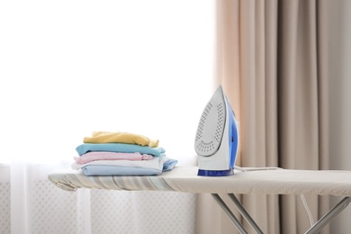 Photo of Board with modern iron and clean clothes indoors. Laundry day