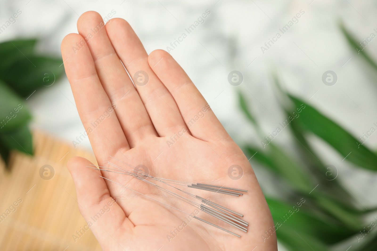 Photo of Woman holding many acupuncture needles on blurred background, top view