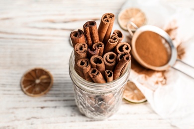 Photo of Jar with aromatic cinnamon sticks on wooden background