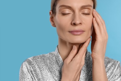 Photo of Woman massaging her face on turquoise background