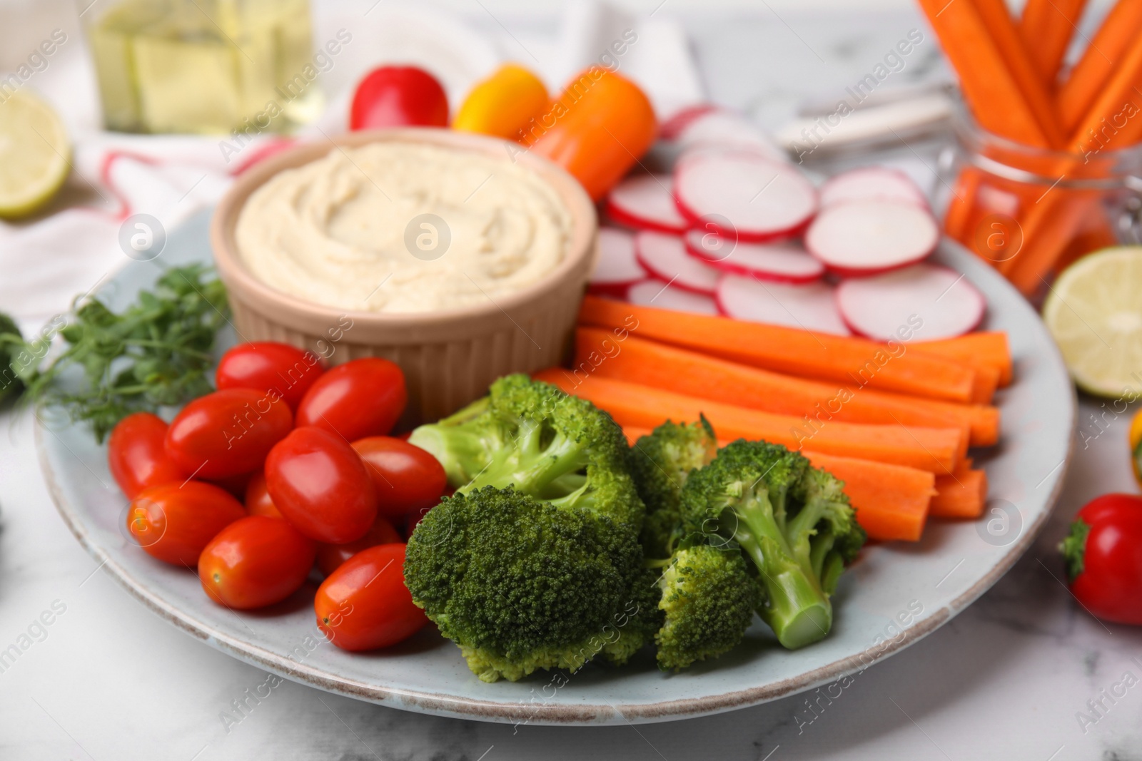 Photo of Plate with delicious hummus and fresh vegetables on white marble table, closeup