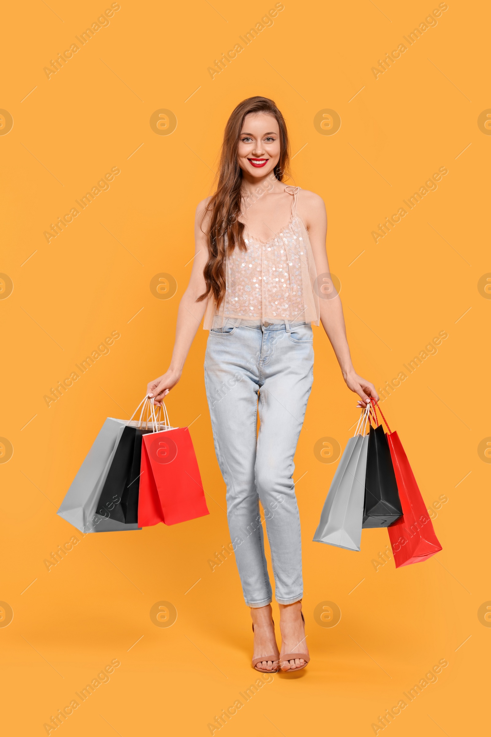 Photo of Stylish young woman with shopping bags on orange background