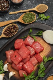 Raw beef meat and different ingredients for cooking delicious goulash on black textured table, flat lay