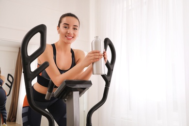 Woman with bottle on modern elliptical machine at home