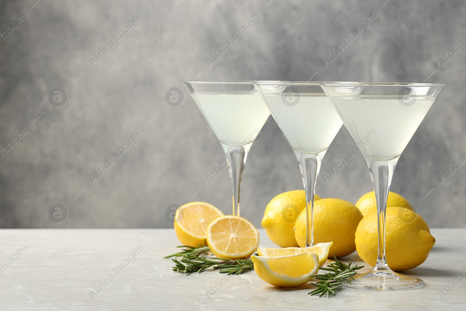 Photo of Martini glasses of refreshing cocktail, lemon and rosemary on light grey textured table. Space for text