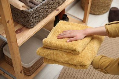 Woman putting towels into storage basket indoors, closeup