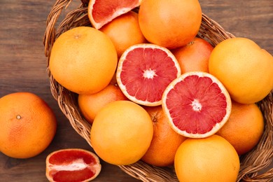 Photo of Wicker basket with fresh grapefruits on wooden table, flat lay
