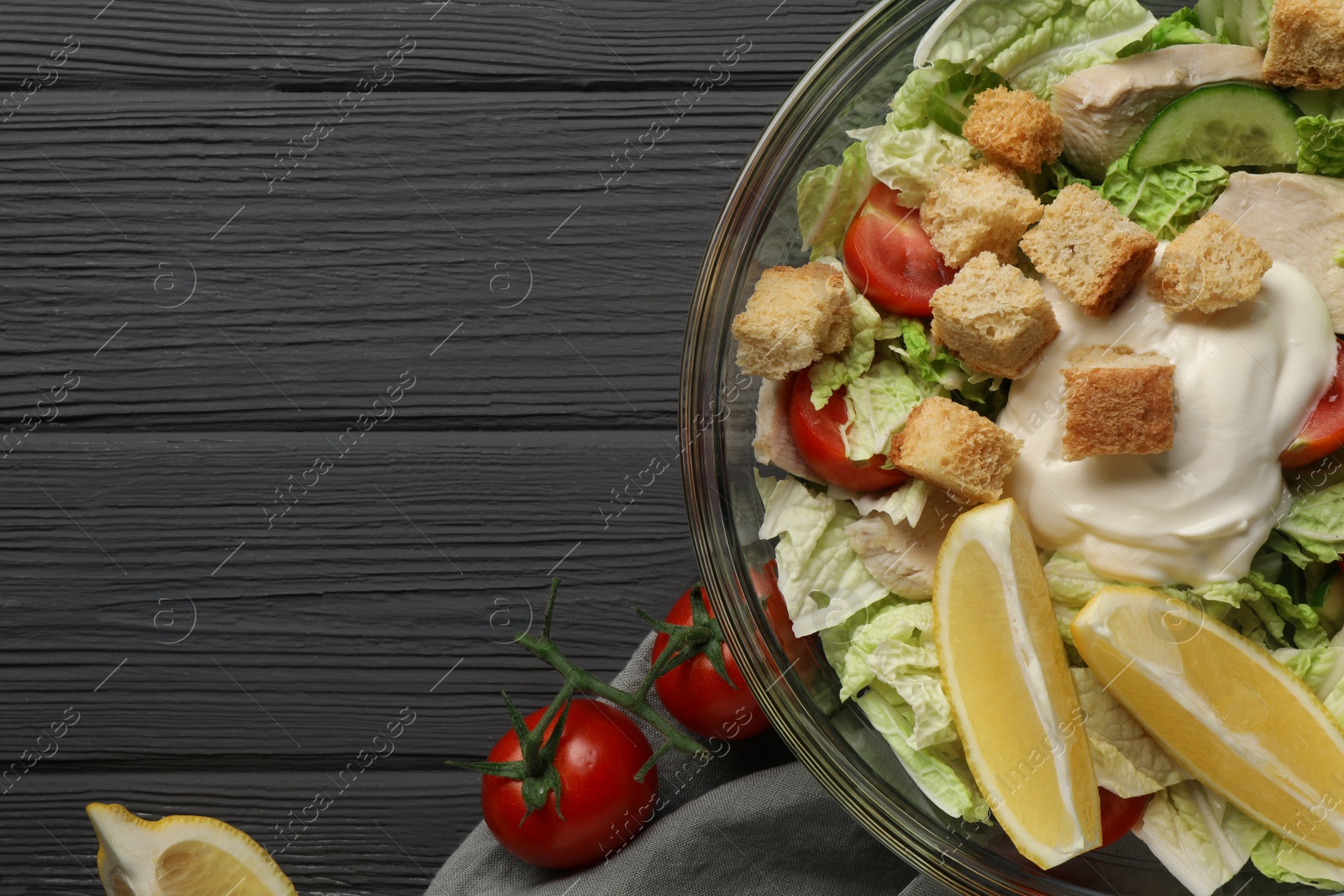 Photo of Bowl of delicious salad with Chinese cabbage, lemon, tomatoes and bread croutons on black wooden table, flat lay. Space for text