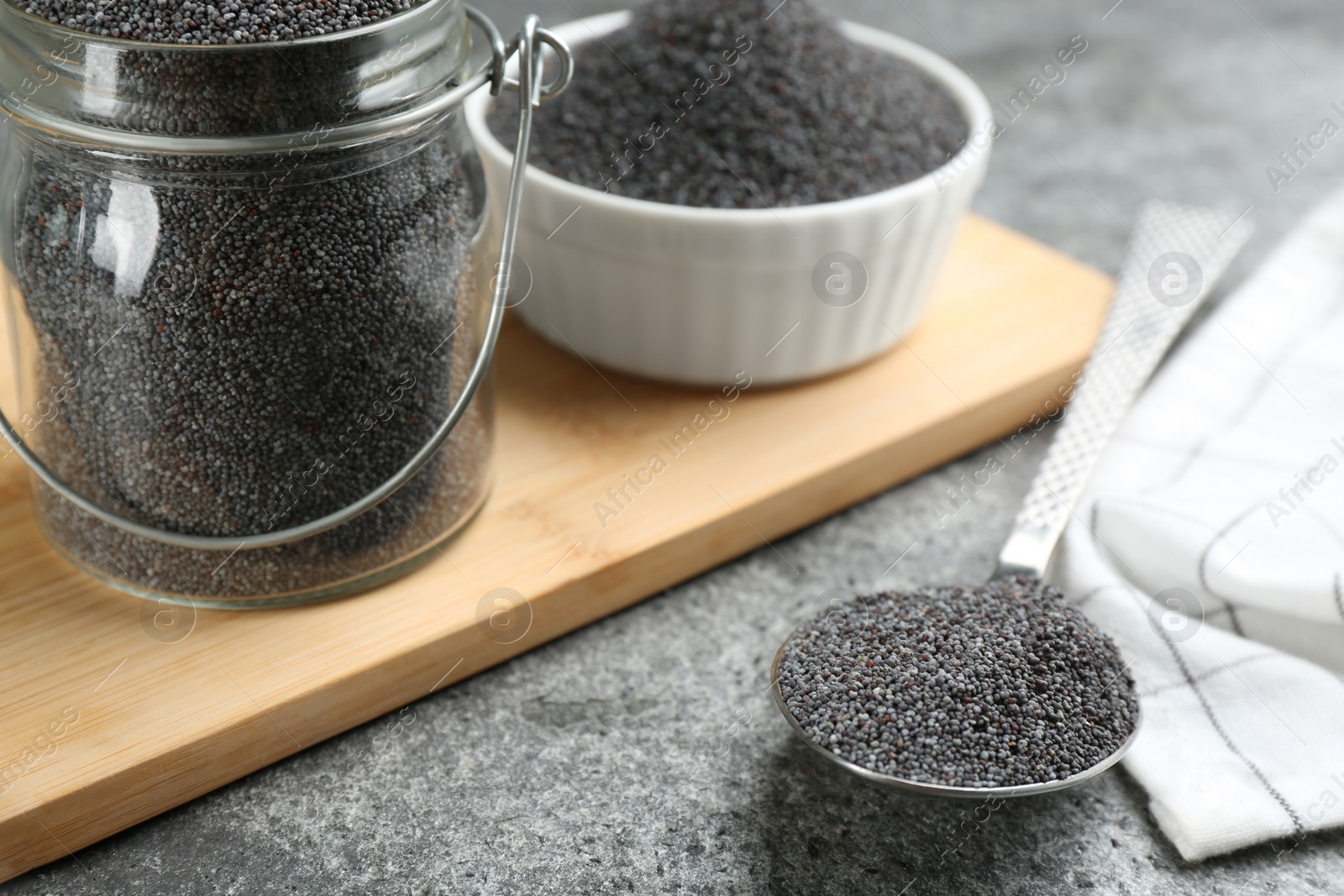 Photo of Poppy seeds in jar and spoon on grey table