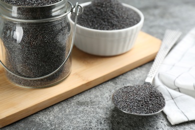 Poppy seeds in jar and spoon on grey table