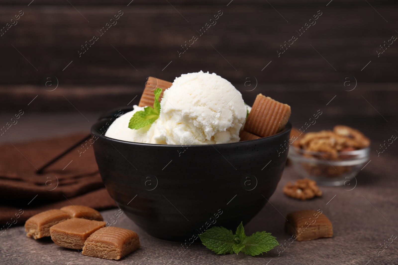 Photo of Tasty ice cream with caramel candies and mint in bowl on brown table, closeup