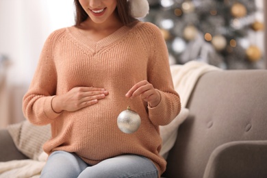 Happy pregnant woman with Christmas ball in living room, closeup. Expecting baby