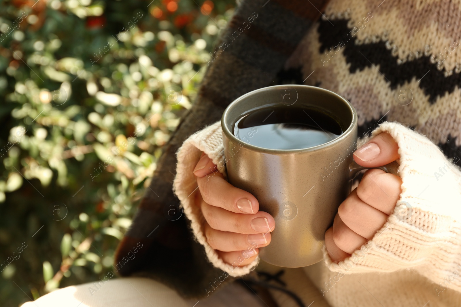 Photo of Woman in cozy sweater with cup of hot drink outdoors on sunny autumn day, closeup