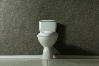 New toilet bowl near grey wall indoors