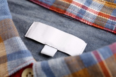 Photo of Blank clothing label on checkered shirt, closeup