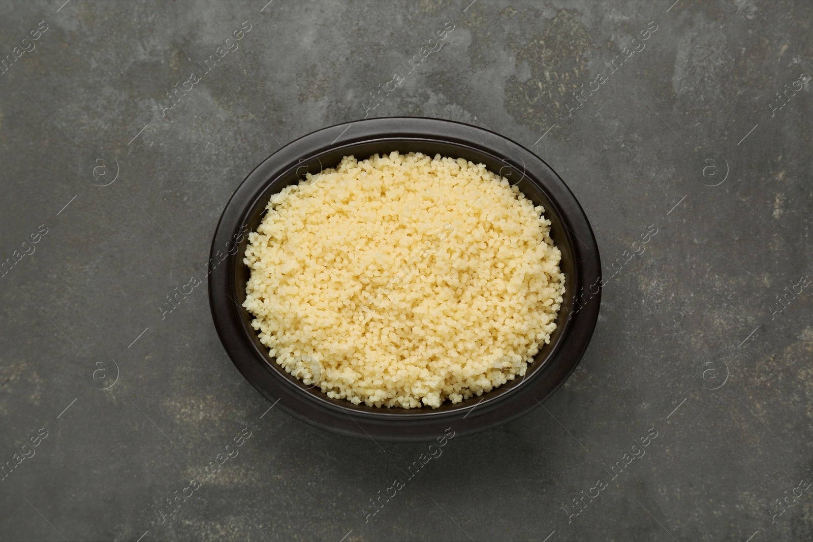 Photo of Bowl of tasty couscous on grey table, top view