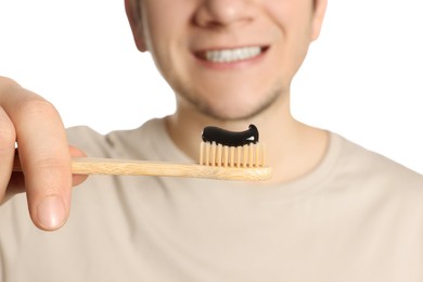 Man holding toothbrush with charcoal toothpaste on white background, closeup