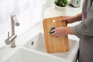 Photo of Man washing wooden cutting board at sink in kitchen, closeup