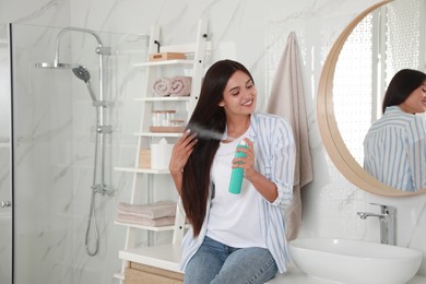 Photo of Woman applying dry shampoo onto her hair near mirror in bathroom