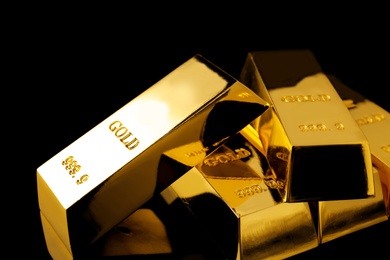 Photo of Many shiny gold bars on black background, closeup