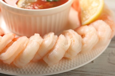 Photo of Tasty boiled shrimps with cocktail sauce and lemon on white wooden table, closeup