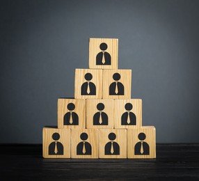 Image of Team and management concept. Pyramid of wooden cubes with human icons on table against grey background