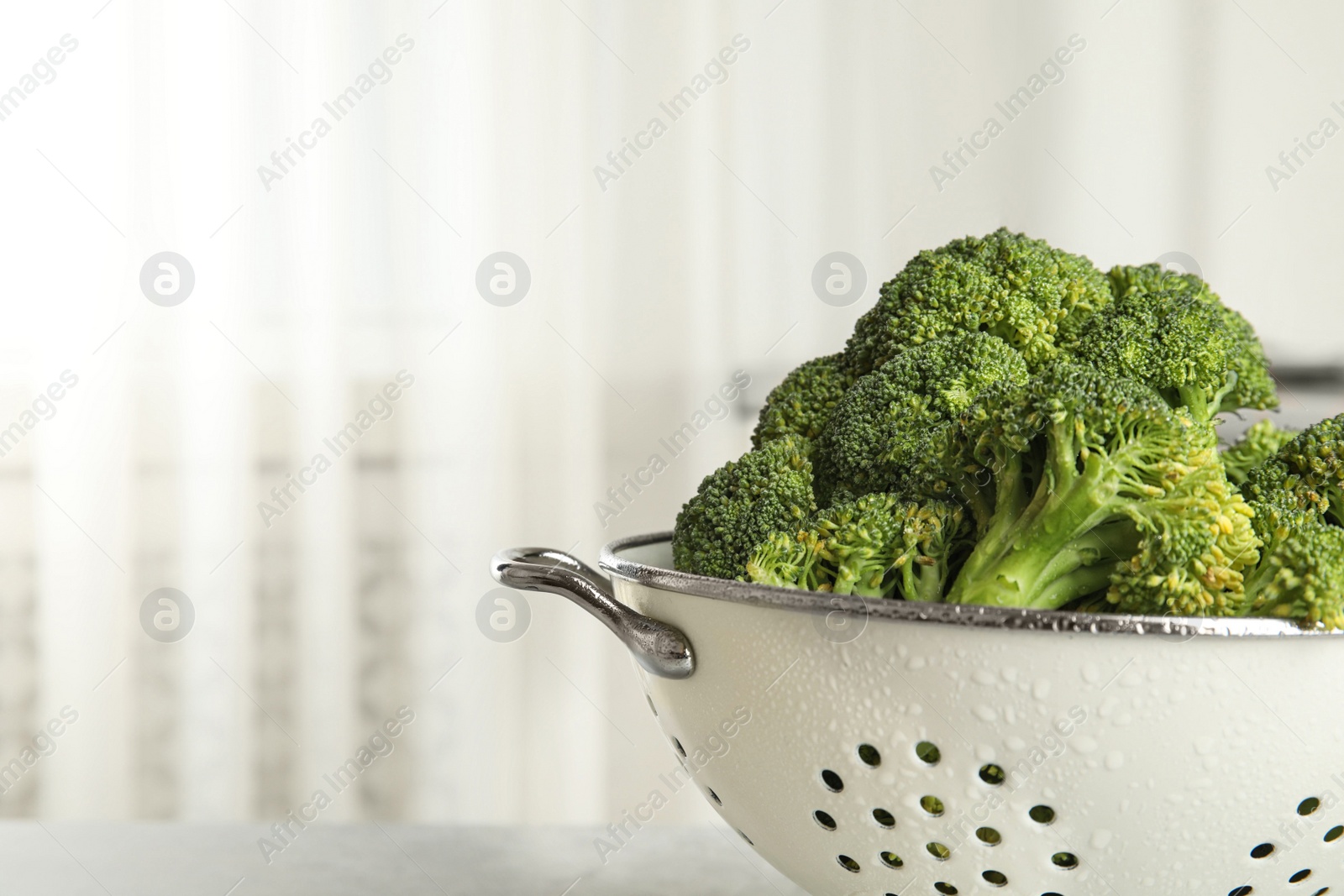 Photo of Raw green broccoli in colander on light background, closeup. Space for text