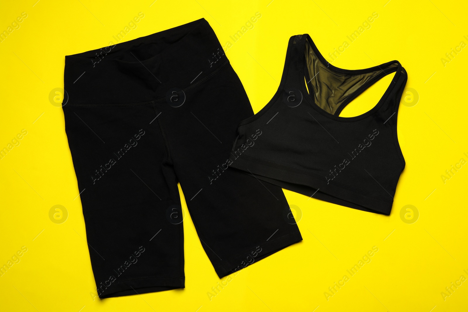 Photo of New black sportswear on yellow background, flat lay