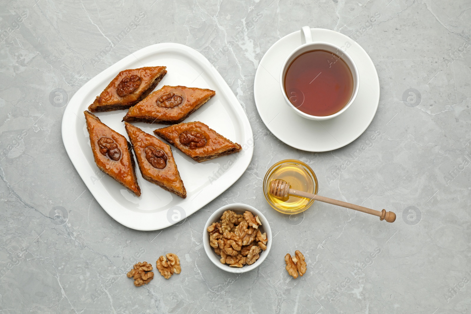 Photo of Delicious sweet baklava with walnuts, honey and hot tea on light grey marble table, flat lay