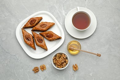 Delicious sweet baklava with walnuts, honey and hot tea on light grey marble table, flat lay