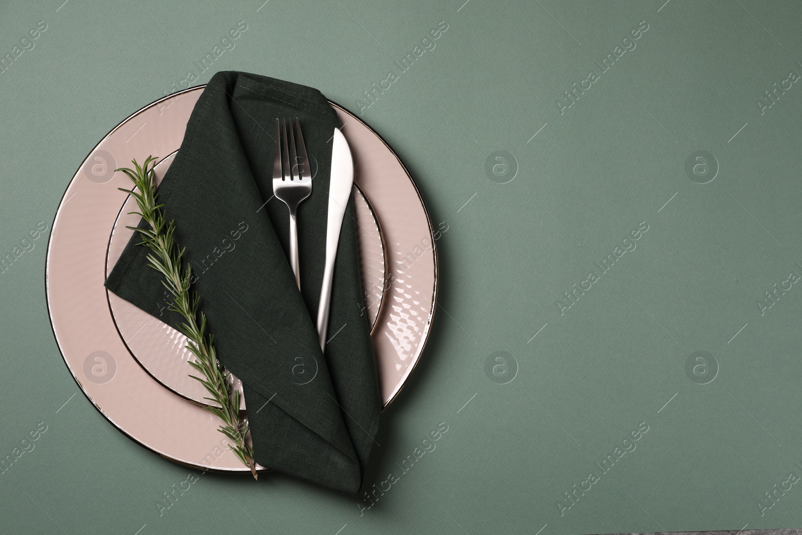 Photo of Stylish table setting. Plates, cutlery, napkin and rosemary on green background, top view with space for text