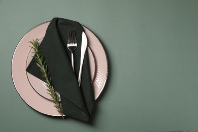 Stylish table setting. Plates, cutlery, napkin and rosemary on green background, top view with space for text