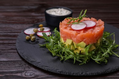 Tasty salmon tartare with radish, avocado and arugula on wooden table, closeup