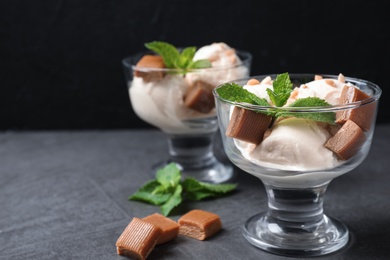 Glass bowls of ice cream with caramel candies and mint on grey table