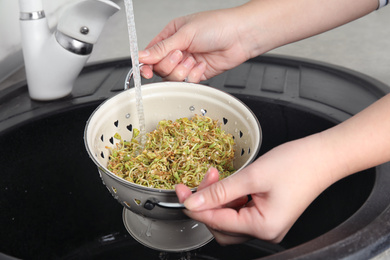 Woman washing sprouted green buckwheat over sink, closeup