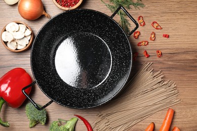 Photo of Empty iron wok surrounded by raw ingredients on wooden table, flat lay