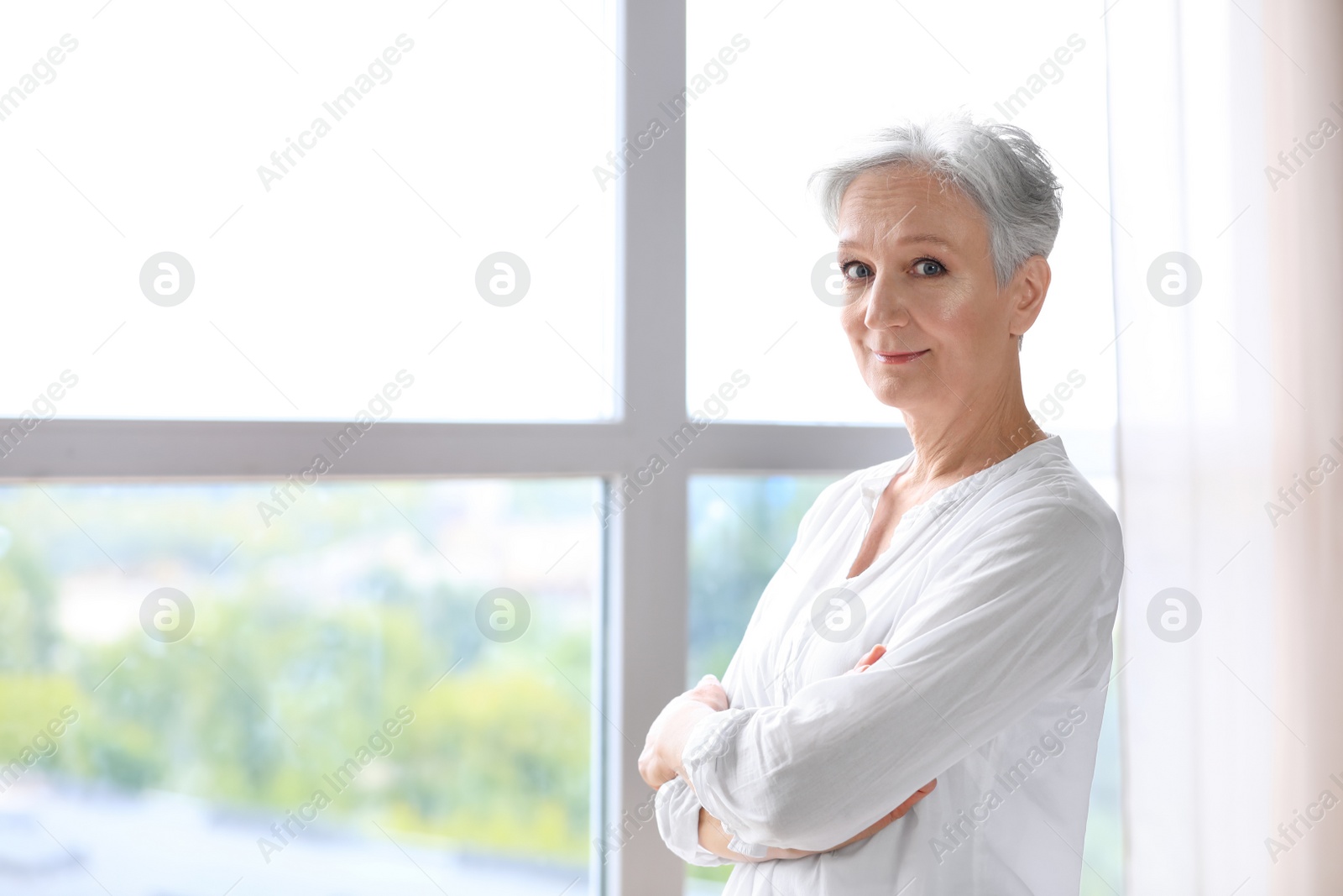 Photo of Happy mature woman near window indoors, space for text. Smart aging