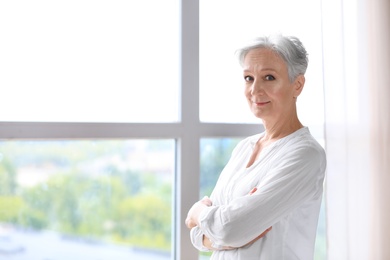 Photo of Happy mature woman near window indoors, space for text. Smart aging