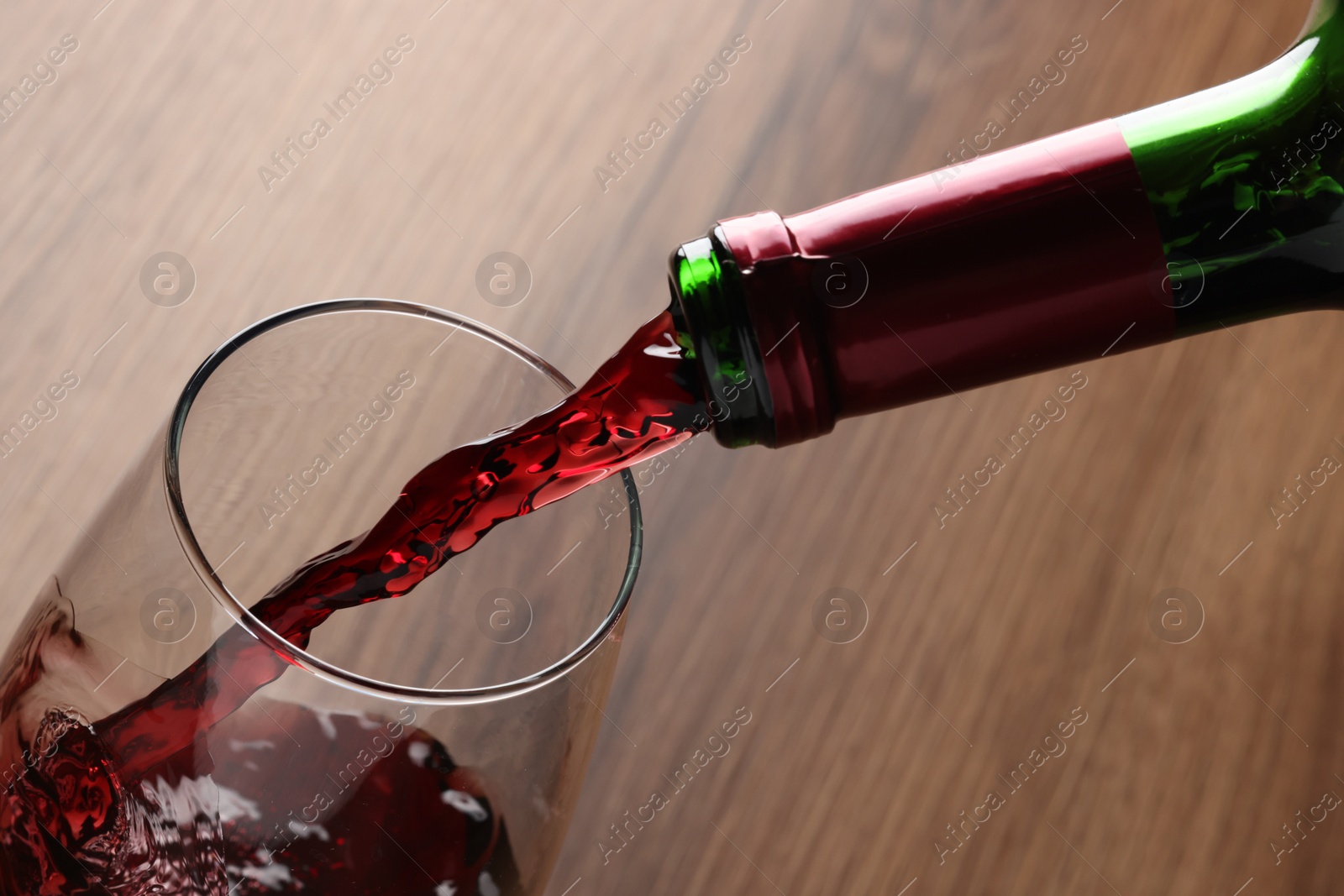 Photo of Pouring tasty red wine in glass at wooden table, closeup