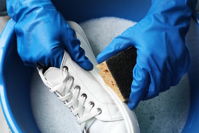 Photo of Woman with gloves and sponge cleaning stylish sneakers in wash basin, top view